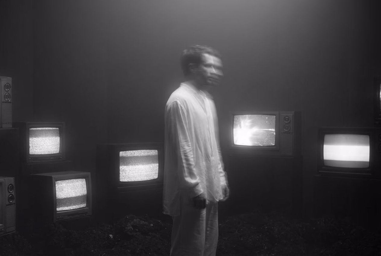 A figure standing among glowing vintage televisions, motion-blurred and monochrome